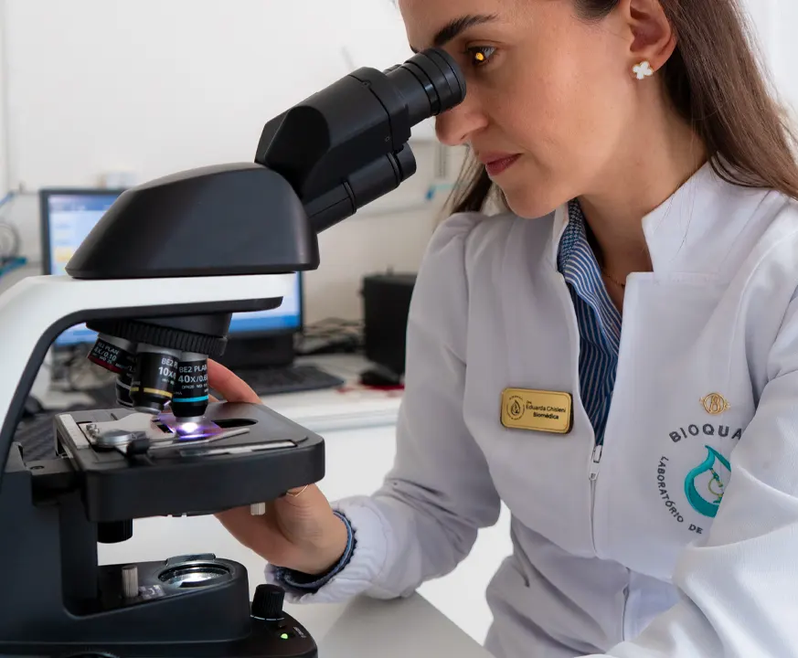 Profissional da BioQuali de jaleco analisando uma amostra ao microscópio no laboratório